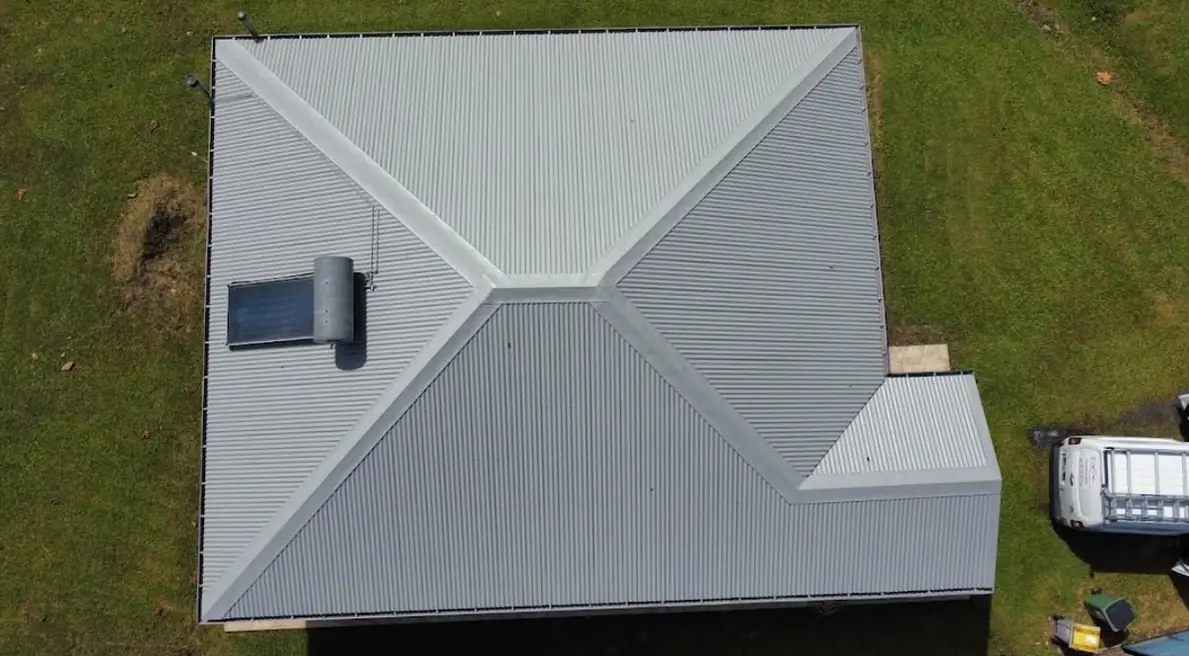Vue aérienne d'une toiture à quatre pans terminée en tôle grise, véhicule de chantier au sol