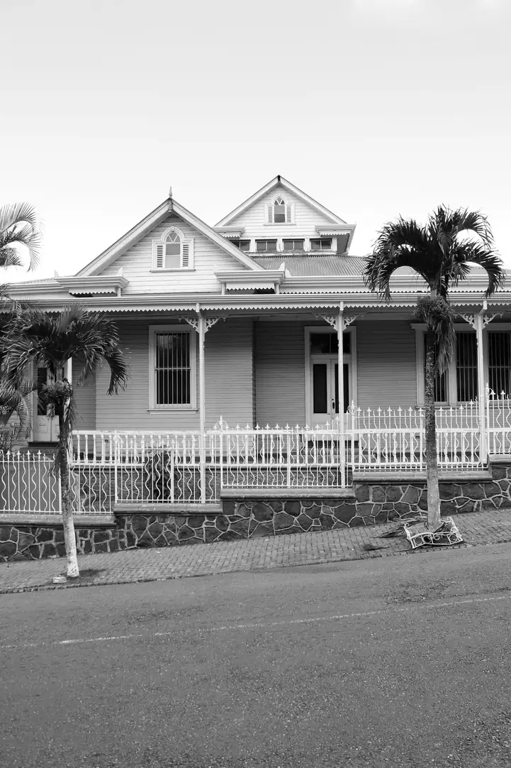 Maison créole à véranda et lucarnes, entourée de palmiers, en noir et blanc