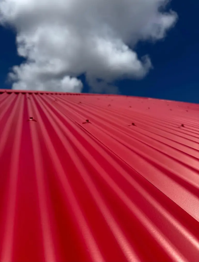 Gros plan sur les ondes d'une tôle rouge neuve et sur ses fixations, ciel bleu